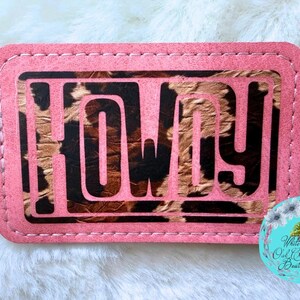 May include: A pink rectangular patch with the word "HOWDY" in black block letters. The letters are set against a brown and tan animal print background. The patch has a stitched border.