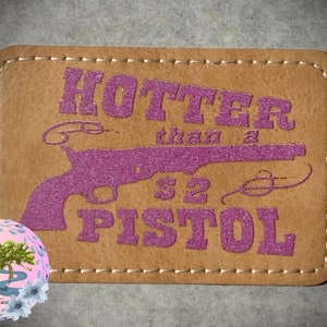 May include: A rectangular, tan leather patch with the text "HOTTER than a S2 PISTOL" in purple. A purple pistol graphic is also featured. The patch has a stitched border and a floral logo in the lower left corner.