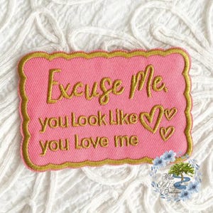 May include: Pink fabric patch with gold embroidered text that reads "Excuse me, you look like you love me". The patch has a gold scalloped border and two gold embroidered hearts.