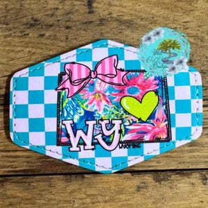 May include: A turquoise and white checkered background with a pink bow and a green heart. The letters "WY" are in pink and black with the word "Wyoming" underneath.