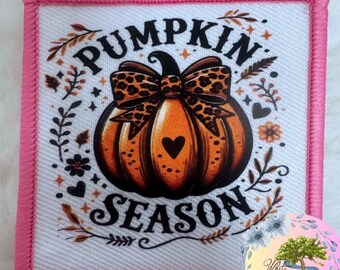 May include: Square patch with a pink border featuring a pumpkin design. The pumpkin is orange with a leopard print bow and a heart. The words "PUMPKIN SEASON" are written in black. Floral and leaf accents surround the pumpkin.