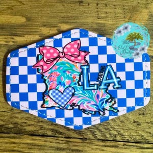 May include: A blue and white checkered fabric patch with a pink bow, a blue heart, and the outline of the state of Louisiana with the text "LA LOUISIANA" on it.