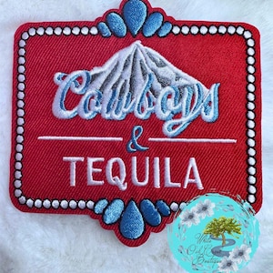 May include: A red embroidered patch with the words "Cowboys & Tequila" in white and blue script. The patch has a white border with small dots and blue teardrop-shaped accents at the top and bottom.