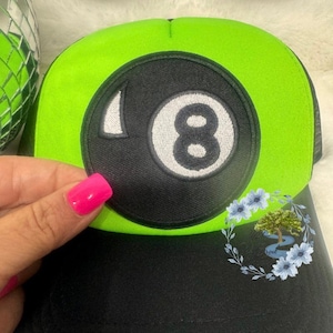 May include: A black and green trucker hat with a black and white 8-ball patch on the front.
