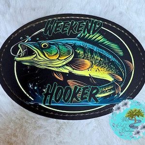 May include: Oval patch with a neon-style illustration of a fish with the words "WEEKEND HOOKER" in green. The fish is blue, yellow, and orange, with a fishing hook in its mouth, set against a black background.