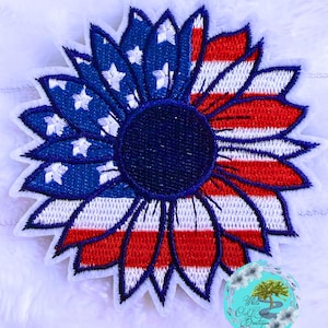 May include: Embroidered sunflower patch with a patriotic design. The petals are split, with one half featuring the American flag's stars and stripes in red, white, and blue. The center is a dark blue circle.