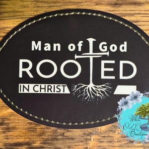 May include: Black oval patch with white text that reads "Man of God Rooted in Christ". A white stylized cross with a tree root design is centered on the patch.