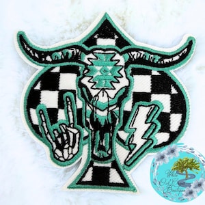 May include: Embroidered patch featuring a bull skull design with a turquoise and black color scheme. The patch includes a checkered background, a hand gesture, and a lightning bolt. The patch is bordered with a turquoise outline.