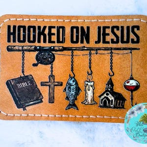 May include: A tan leather patch with the words "HOOKED ON JESUS" in bold black letters. Below, a fishing rod suspends a Bible, cross, fish, candle, church, and bobber. The patch has a stitched border.