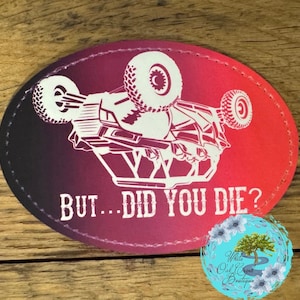 May include: An oval patch with a gradient background of red and black. A white graphic of a vehicle flipped upside down is in the center. The text "BUT... DID YOU DIE?" is below the vehicle. A small circular logo is in the bottom right corner.