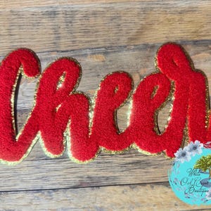 May include: Red felt "Cheer" patch with gold glitter trim. The patch is perfect for adding a touch of school spirit to clothing, bags, or crafts.