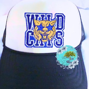May include: A black and white trucker hat with a white front panel. The front features the text "WILDCATS" in blue, with a gold and blue wildcat graphic. The brim is black, and the hat has a mesh back.
