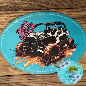May include: A light blue oval patch featuring a black and white off-road vehicle splashing through mud. The text "SIDE CHICK" is in pink. A small circular logo with a tree and the text "White Oak Creek Boutique" is in the bottom right corner.