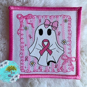 May include: Embroidered square patch featuring a cartoon ghost with a pink ribbon, bow, and flowers. The patch has a pink border and a striped background. The ghost is holding a pink ribbon, symbolizing breast cancer awareness.