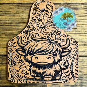 May include: A brown leather key chain with a black and white paisley design and a black and white cartoon highland cow.