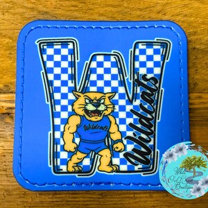 May include: A blue square coaster with a white and blue checkered "W" design. A cartoon wildcat in a blue uniform is in the center. The word "Wildcats" is written in black script. The coaster has a blue border.