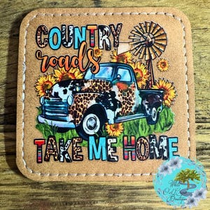 May include: A brown leather coaster with a vintage truck, sunflowers, and a windmill. The text "COUNTRY roads TAKE ME HOME" is printed on the coaster.