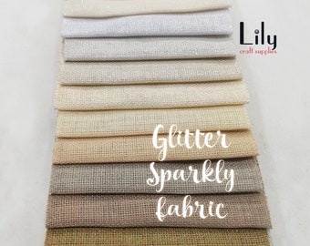 May include: A stack of 14 different colours of sparkly fabric with a glittery finish. The fabric is arranged in a gradient from white to gold. The text "Glitter Sparkly Fabric" is printed on the fabric.