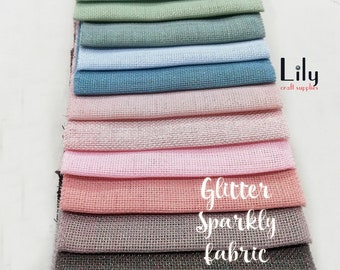 May include: A stack of 14 different colors of sparkly fabric with a subtle glitter finish. The fabric is a woven material with a slightly textured surface. The fabric is labeled "Glitter Sparkly Fabric".