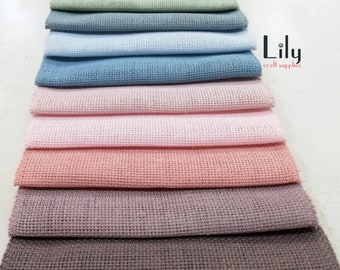May include: A stack of 12 different colored Aida cloth fabric squares. The colors are brown, green, light blue, blue, pink, light pink, purple, gray, and black. The fabric is a popular choice for cross stitch and needlepoint projects.