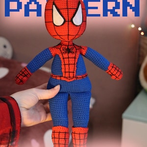 May include: A crocheted Spider-Man amigurumi doll. The doll is primarily blue and red, with white eye accents. The text "CROCHET PATTERN" is displayed at the top, with "PDF" and "Amigurumi" at the bottom.