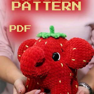 May include: A red crocheted strawberry-shaped plush toy with black eyes and a green stem. The toy has yellow seed details and is held in someone's hands. The image includes the text "CROCHET PATTERN PDF".