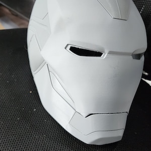 Op de afbeelding: Een wit, ongeverfd Iron Man-masker van plastic met een gedetailleerd ontwerp. Het masker heeft een reliëf, textuur en twee ooggaten.