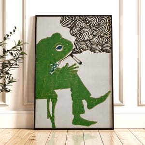 May include: A framed art print featuring a green frog in a suit, smoking a cigarette. The frog is seated, with a blue eye and a patterned bow tie. The smoke is depicted in black and white swirls.