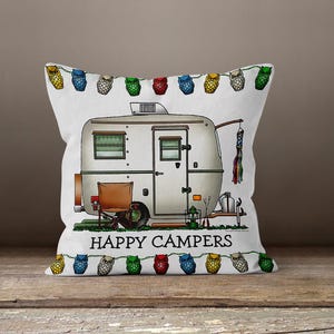 May include: White square pillow with a cartoon illustration of a vintage camper. The camper is gray with a brown chair and a string of owl-shaped lights. The text "HAPPY CAMPERS" is printed below the camper.