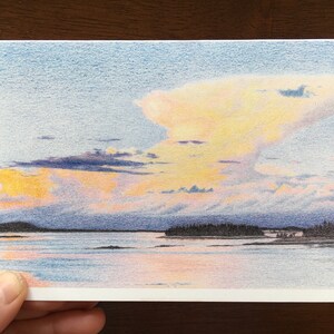Peut inclure: Un dessin au crayon représentant un coucher de soleil sur une étendue d'eau avec une petite île au loin. Le ciel est un mélange de rose, d'orange et de jaune, avec des nuages de formes et de tailles variées. L'eau est d'un bleu calme, reflétant les couleurs du ciel.