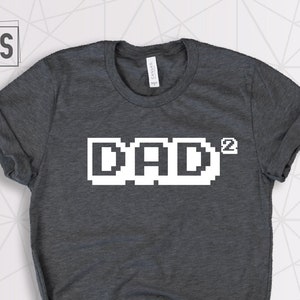 May include: Dark grey t-shirt with a white pixelated graphic that says "DAD^2".