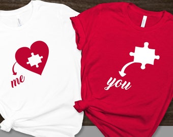 Puede incluir: Dos camisetas con un diseño de corazón de pieza de rompecabezas. La camiseta blanca dice "yo" y la camiseta roja dice "tú".
