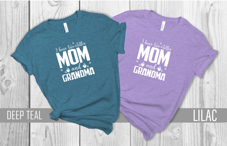May include: Two t-shirts with the text "I have two titles MOM and GRANDMA" printed on them. The shirt on the left is teal and the shirt on the right is lilac.