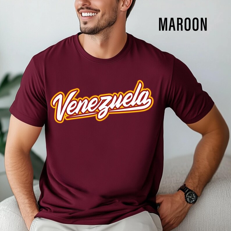 May include: Maroon t-shirt with the word "Venezuela" in a white script font with a gold outline. The shirt is short-sleeved and made of a soft material.