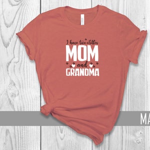 May include: A mauve t-shirt with the text "I have two titles MOM and GRANDMA" in white with black paw prints and hearts.