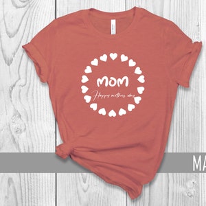 May include: A mauve t-shirt with a white circle design featuring the word "MOM" and the text "Happy Mother's Day" surrounded by white hearts.