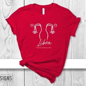 May include: Red t-shirt with a white Libra zodiac symbol and the text "Positive Person & Kind".