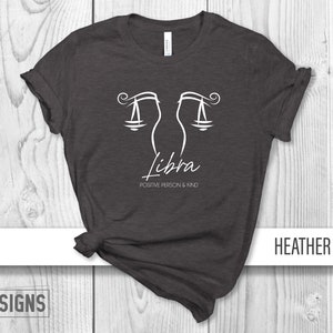 May include: Heather dark grey t-shirt with a white Libra zodiac symbol and the text "Positive Person & Kind".