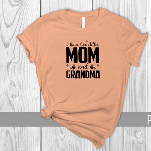 May include: Peach colored t-shirt with black text that reads "I have two littles MOM and GRANDMA" with paw prints and hearts around the text.
