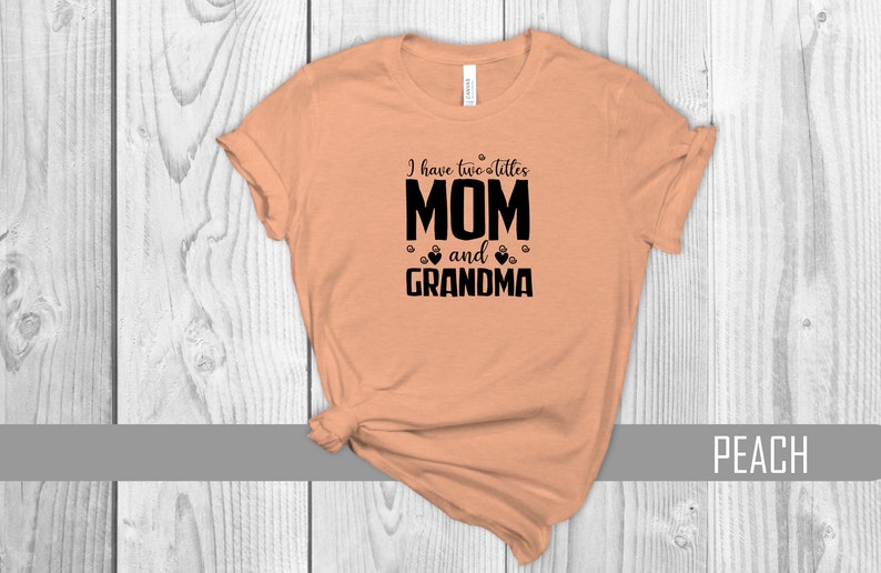 May include: Peach colored t-shirt with black text that reads "I have two littles MOM and GRANDMA" with paw prints and hearts around the text.