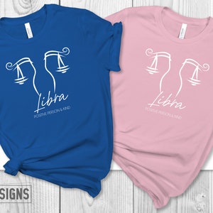 May include: Two t-shirts, one royal blue and one rose, with a white Libra zodiac symbol and the text "Libra, Positive Person & Kind".