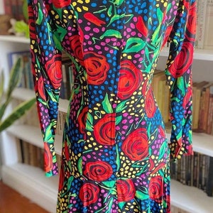 May include: A long-sleeved dress with a black background and a colorful floral pattern. The dress has a fitted bodice and a flowing skirt. The flowers are red, yellow, green, and pink.