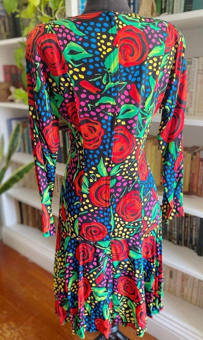 May include: A long-sleeved dress with a black background and a colorful floral pattern. The dress has a fitted bodice and a flowing skirt. The flowers are red, yellow, green, and pink.