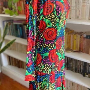 May include: A black dress with a colorful floral print featuring red, pink, yellow, and green roses on a black background. The dress has a scoop neck and long sleeves.
