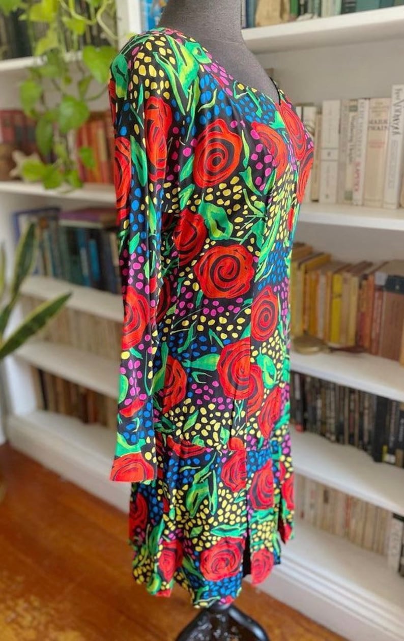 May include: A black dress with a colorful floral print featuring red, pink, yellow, and green roses on a black background. The dress has a scoop neck and long sleeves.