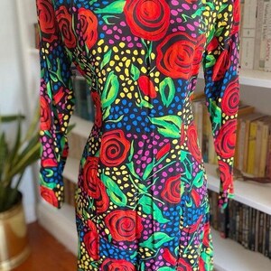 May include: A long-sleeved dress with a black background and a colorful floral print. The print features large red roses, green leaves, and yellow, blue, and pink polka dots.