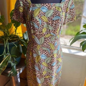 Puede incluir: Un vestido estampado en marr&oacute;n, verde y azul con escote cuadrado y mangas cortas. El vestido tiene una base de estampado de leopardo con un dise&ntilde;o de hojas.