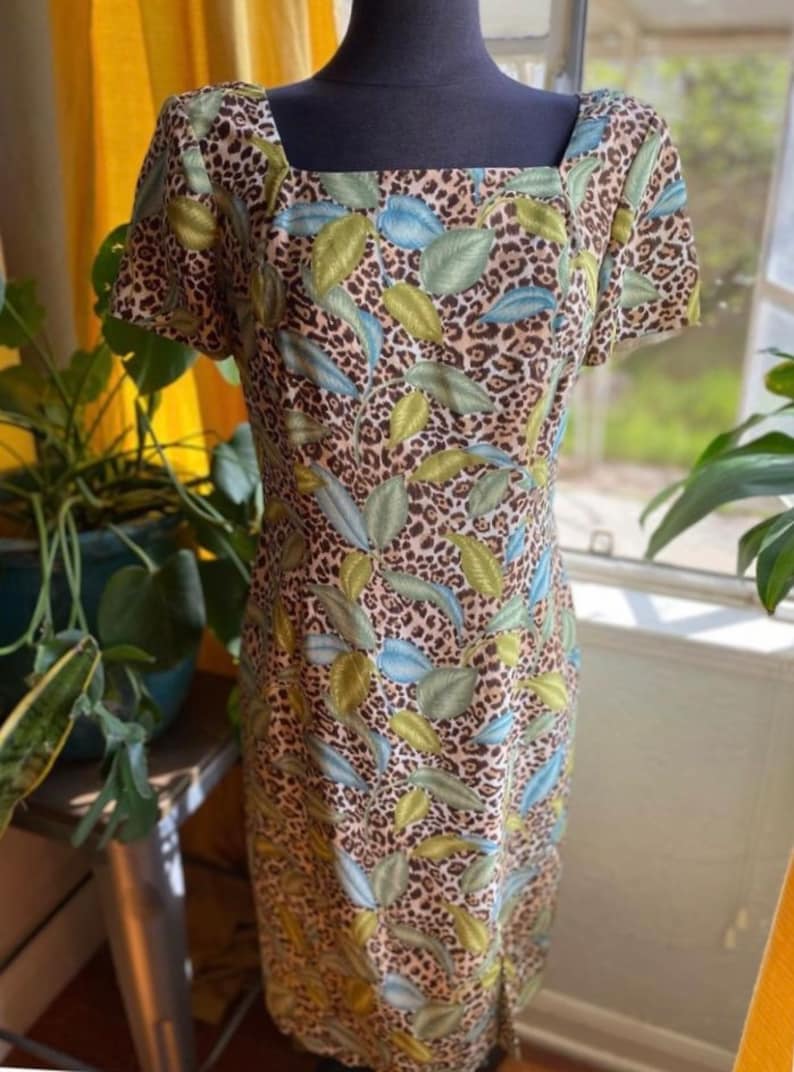 Puede incluir: Un vestido estampado en marr&oacute;n, verde y azul con escote cuadrado y mangas cortas. El vestido tiene una base de estampado de leopardo con un dise&ntilde;o de hojas.