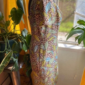 Puede incluir: Un vestido marr&oacute;n y blanco con un estampado de hojas verdes y azules. El vestido tiene una silueta ajustada y un escote cuadrado.