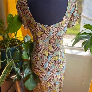 Puede incluir: Un vestido de color marr&oacute;n, verde y azul con estampado de leopardo, cuello redondo y mangas cortas. El vestido es ajustado y tiene una longitud midi.